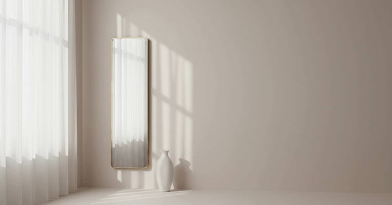 Halbtransparente Gardine vor einem Fenster diffundiert Tageslicht, ein schlanker Wandspiegel und eine weiße Keramikvase verstärken die Lichtlenkung.